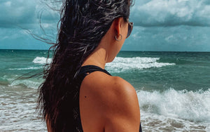 Woman reflecting and standing on the beach looking out into the ocean