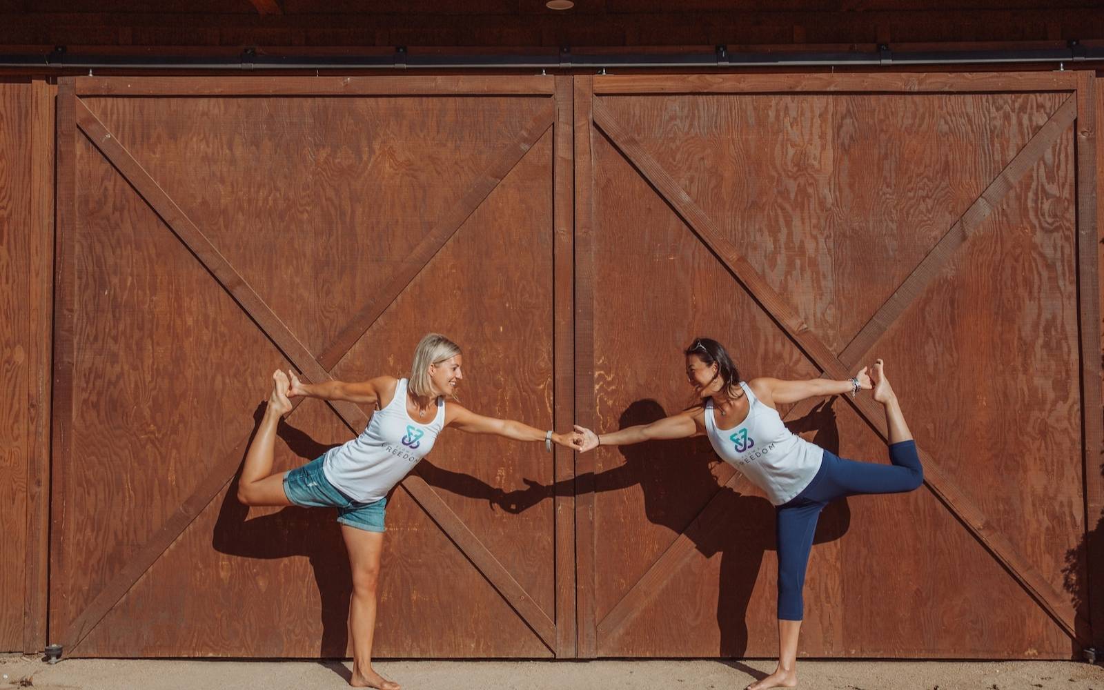 two women holding hands wearing flow 2 freedom aspire tank tops in yoga pose